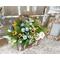 A handmade wooden moose planter. It holds a faux flower arrangement with greenery, peonies, and wildflowers. It sits in an entryway. 